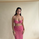 A woman posing indoors in a red and white gingham two-piece set consisting of a bralette top and a matching skirt.
